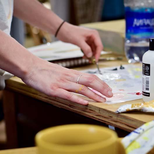A student's hands work with art supplies at a table